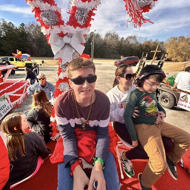 People sitting on a red parade float with red-and-white decorations, smiling outdoors in a field
