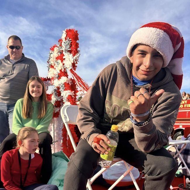 People riding on a festive holiday float, one smiling in a Santa hat and holding a drink.