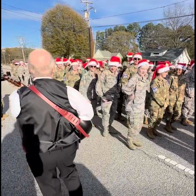 Group of uniformed people in Santa hats marching in a parade on a sunny street