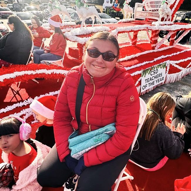 Smiling person in red jacket sitting on a red parade float in a sunny winter scene