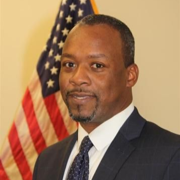 Portrait of a man in a suit standing before a U.S. flag