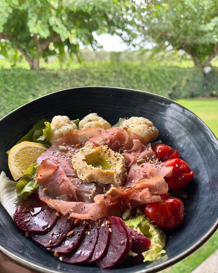 Piatto all'aperto con fette di salmone, patate arrosto, barbabietole, pomodori e limone su un letto di verdure in una ciotola nera.