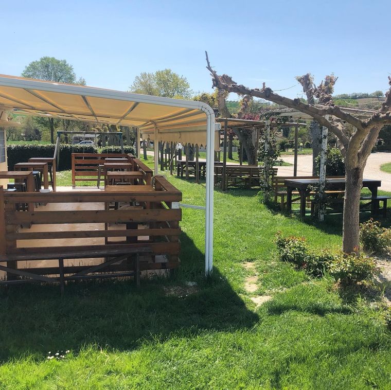 Tavoli da picnic in legno all'aperto, sotto tettoie, in un soleggiato giardino erboso.