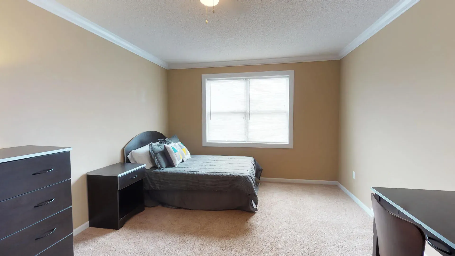A bedroom with a bed , dresser , desk and window.