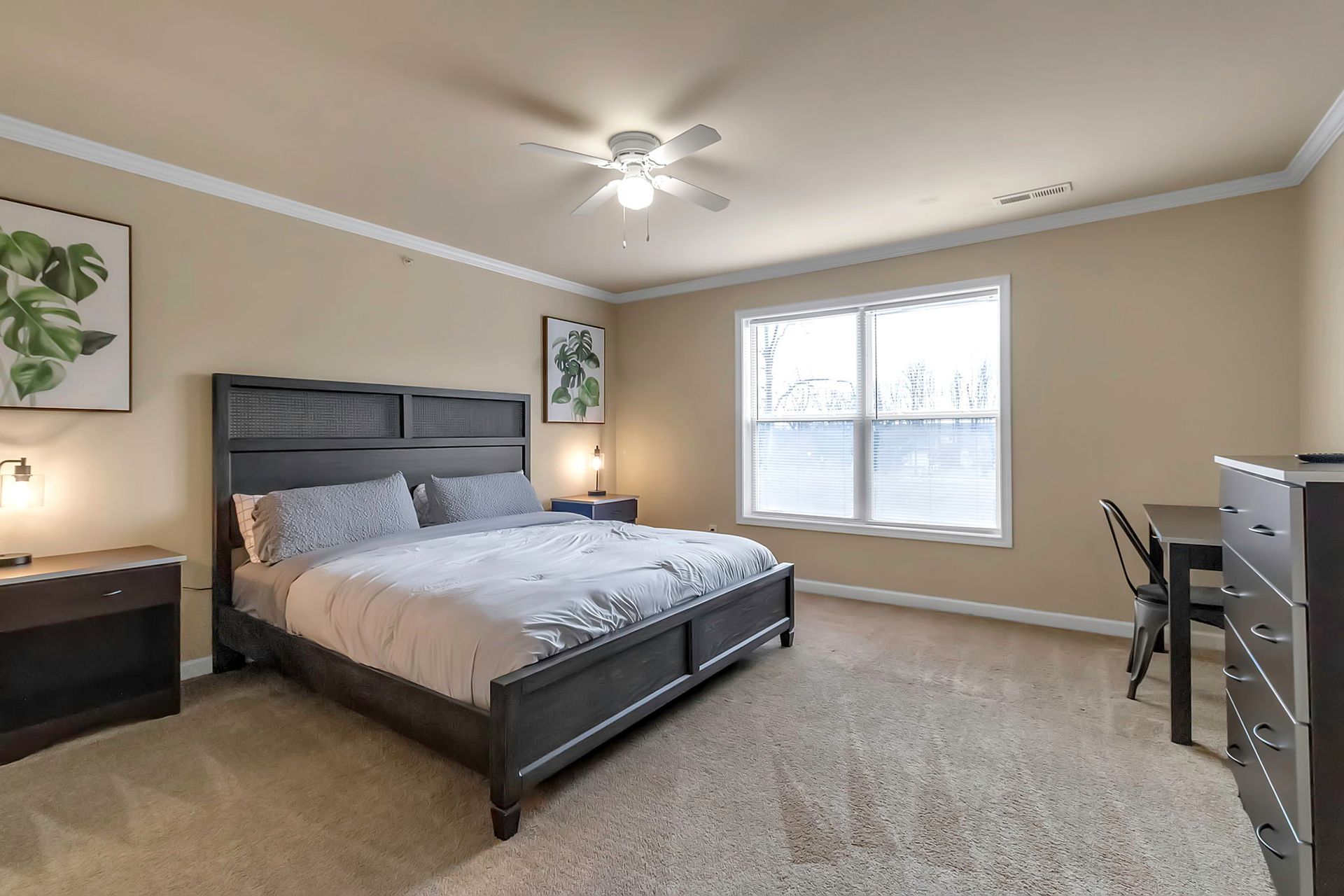 A bedroom with a king size bed , dresser , nightstand , desk and window.