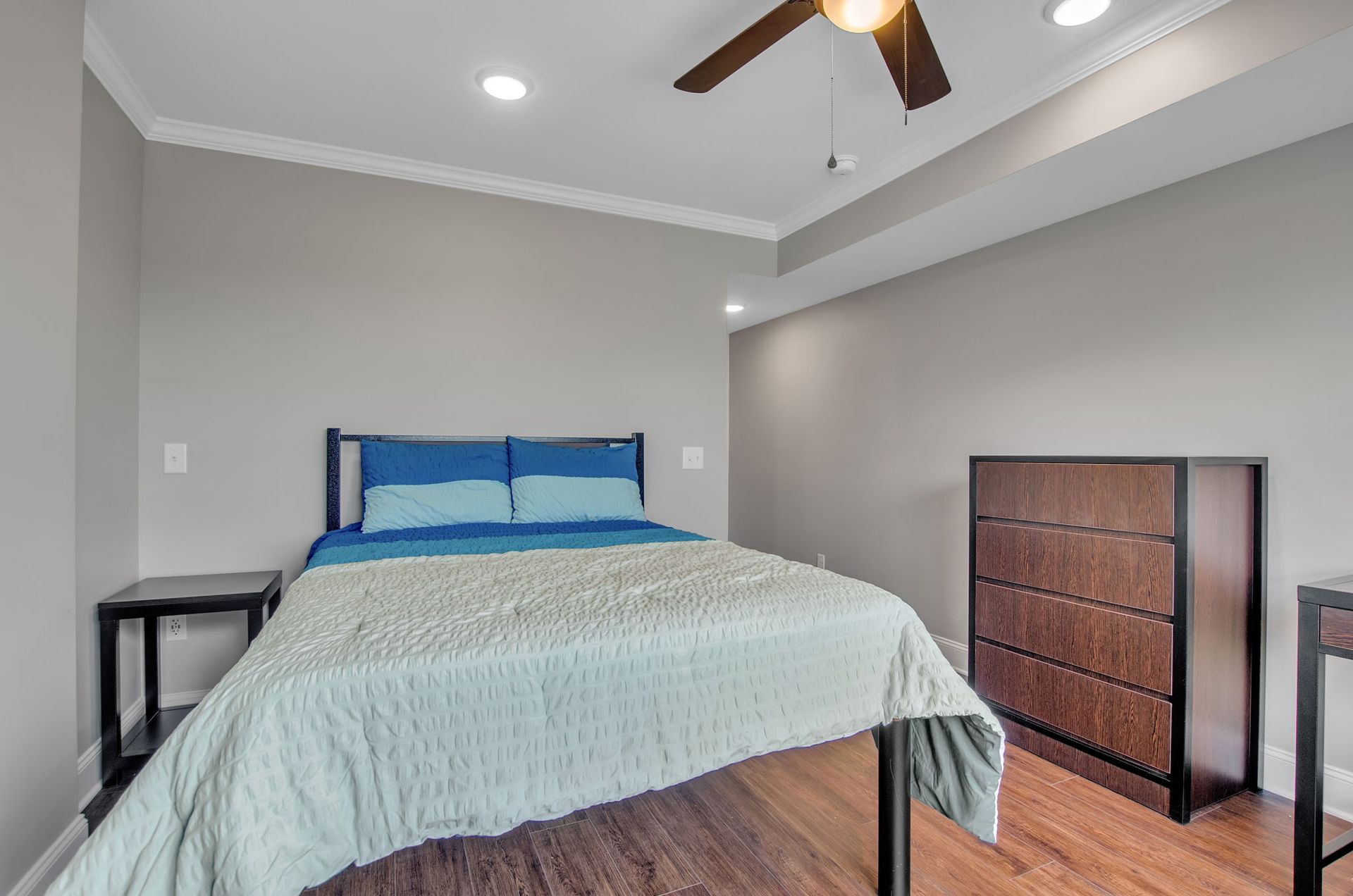 A bedroom with a bed , dresser , nightstand and ceiling fan.