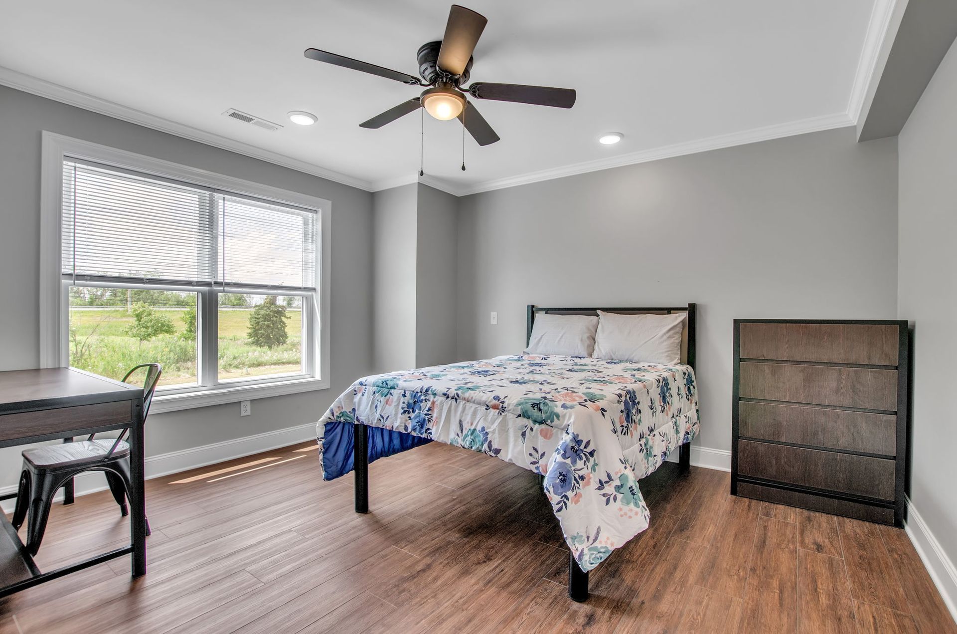 A bedroom with a bed , dresser , desk and ceiling fan.