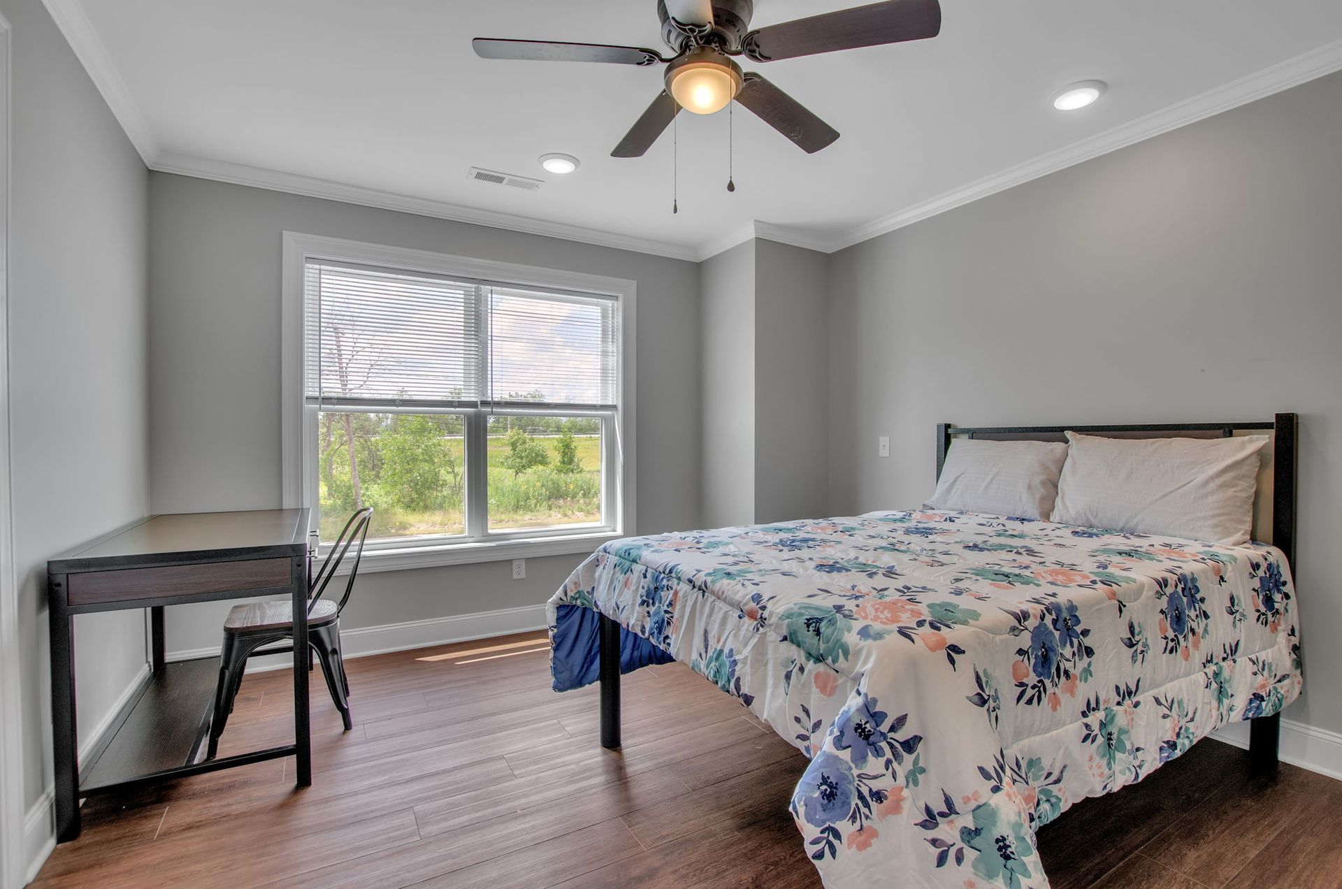 A bedroom with a bed , desk , chair and ceiling fan.