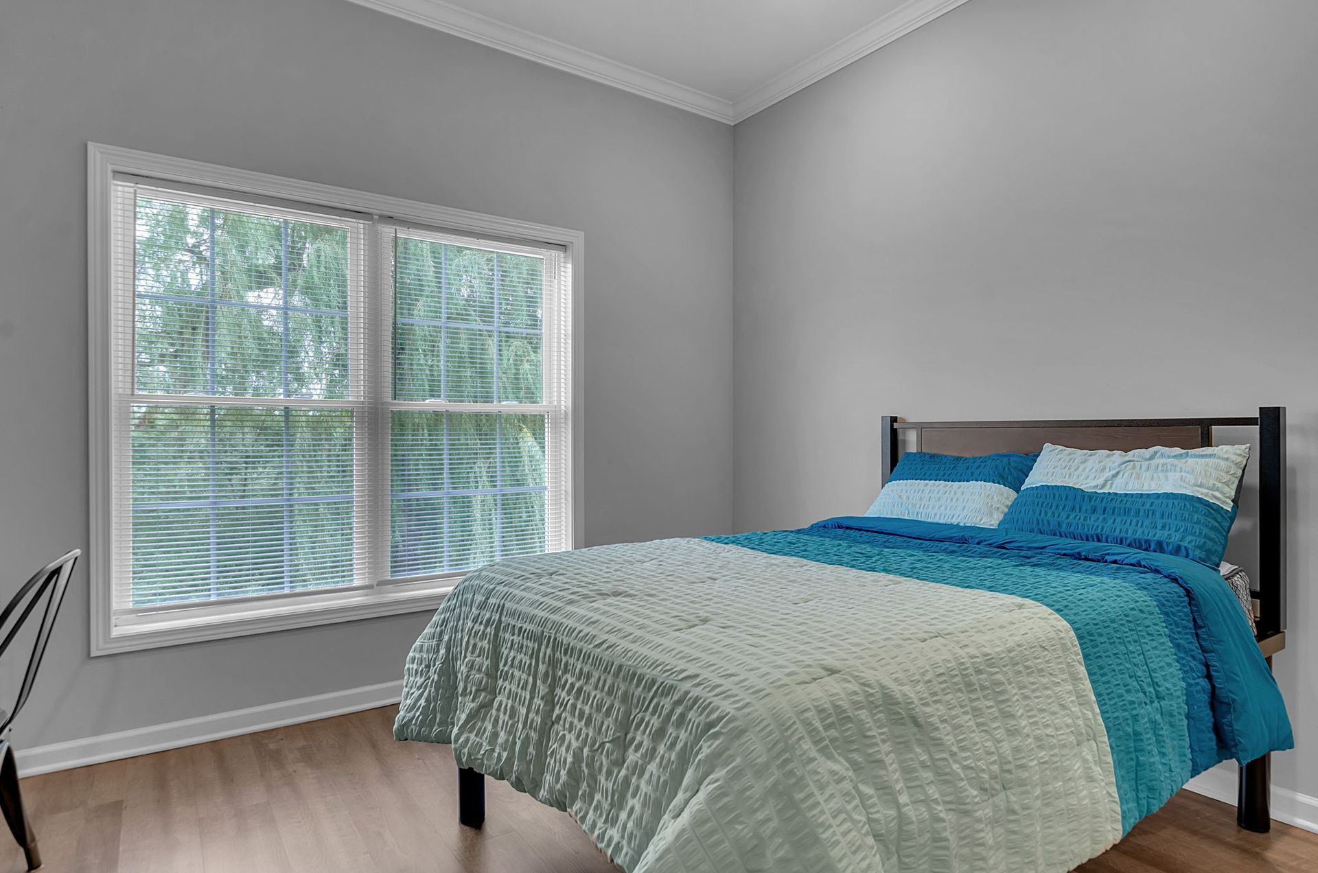 A bedroom with a bed , two windows and hardwood floors.