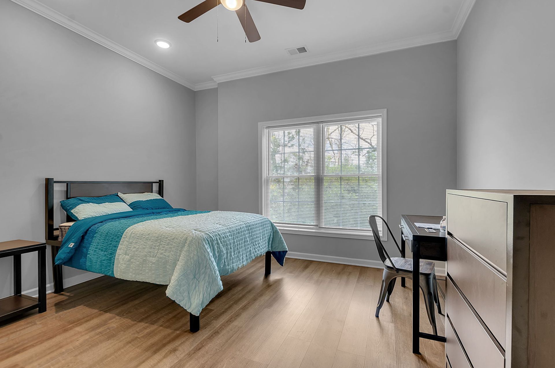 A bedroom with a bed , desk , dresser and ceiling fan.