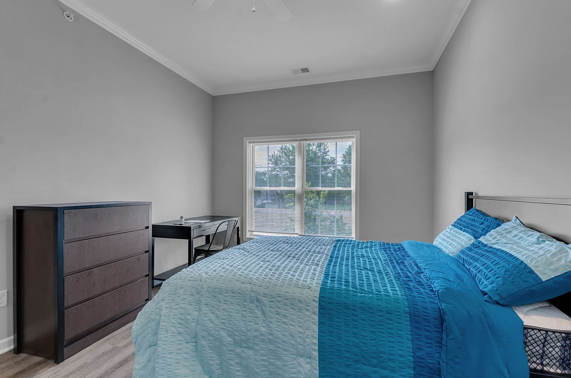 A bedroom with a bed , dresser , desk and window.