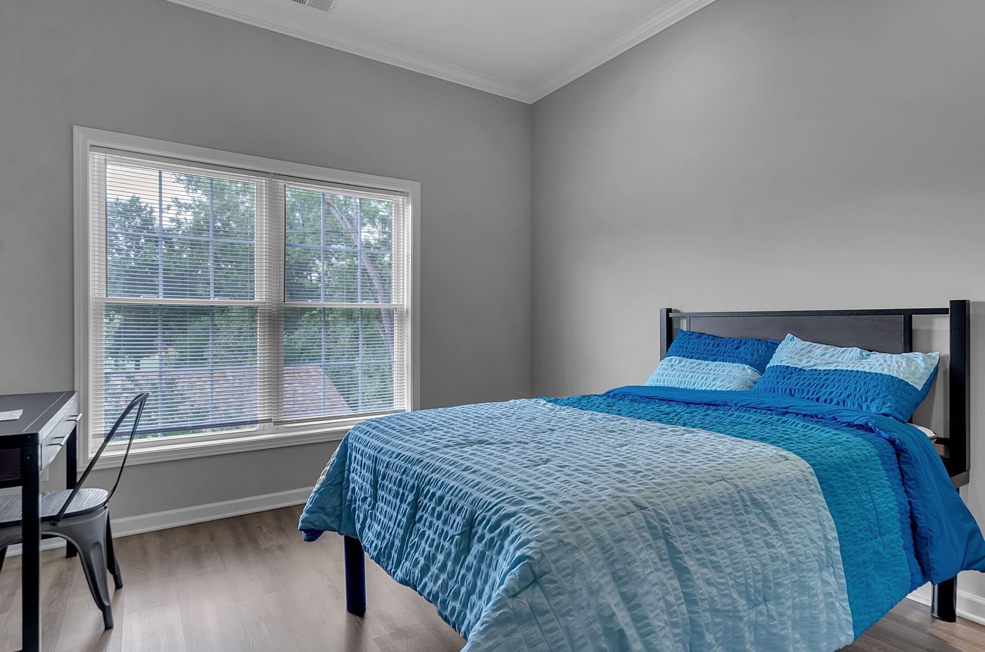 A bedroom with a bed , desk , chair and two windows.