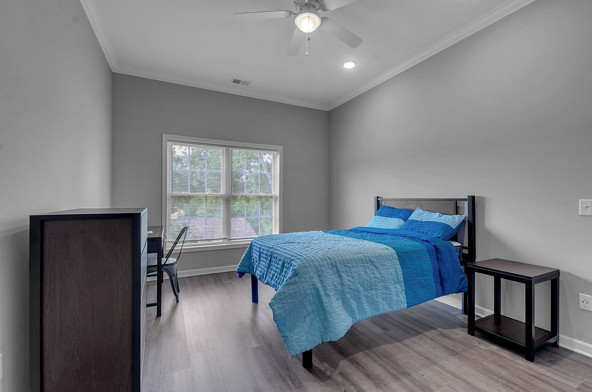 A bedroom with a bed , nightstand , desk and ceiling fan.