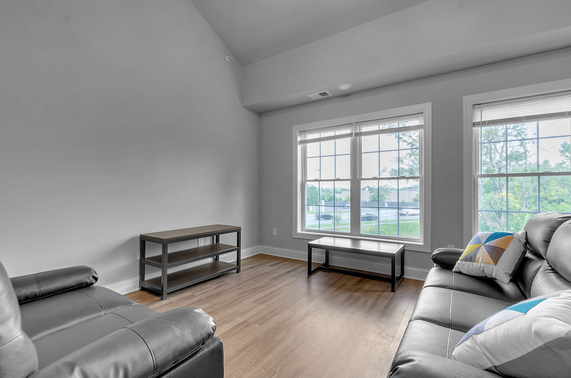 A living room with a couch , chair , coffee table and two windows.