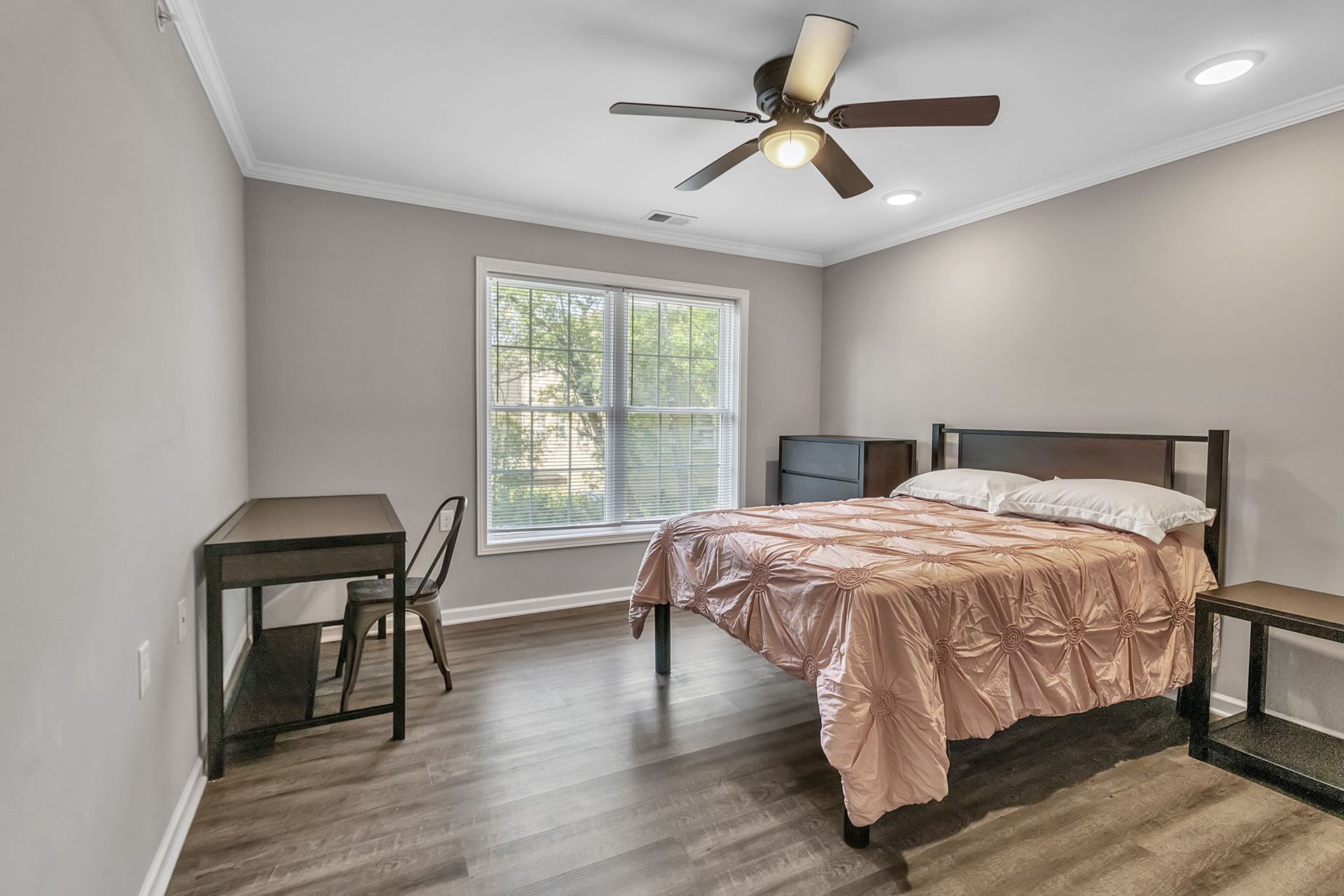 A bedroom with a bed , desk , chair and ceiling fan.