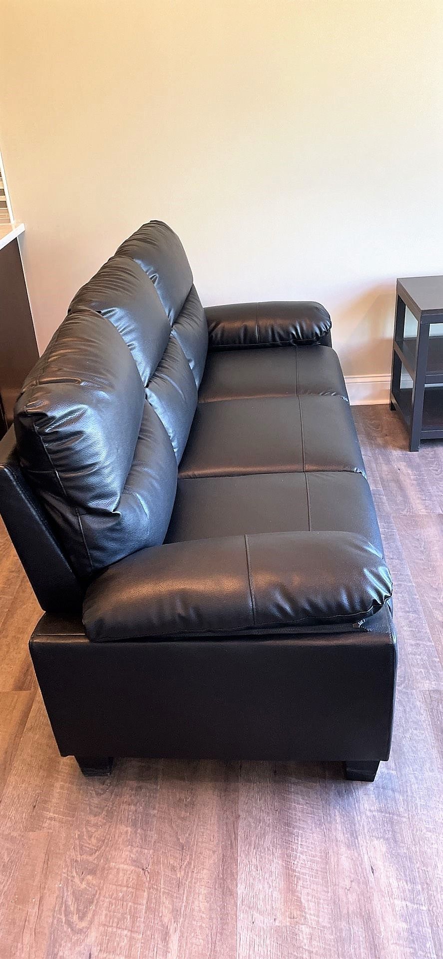 A black leather couch is sitting on a carpet in a living room.