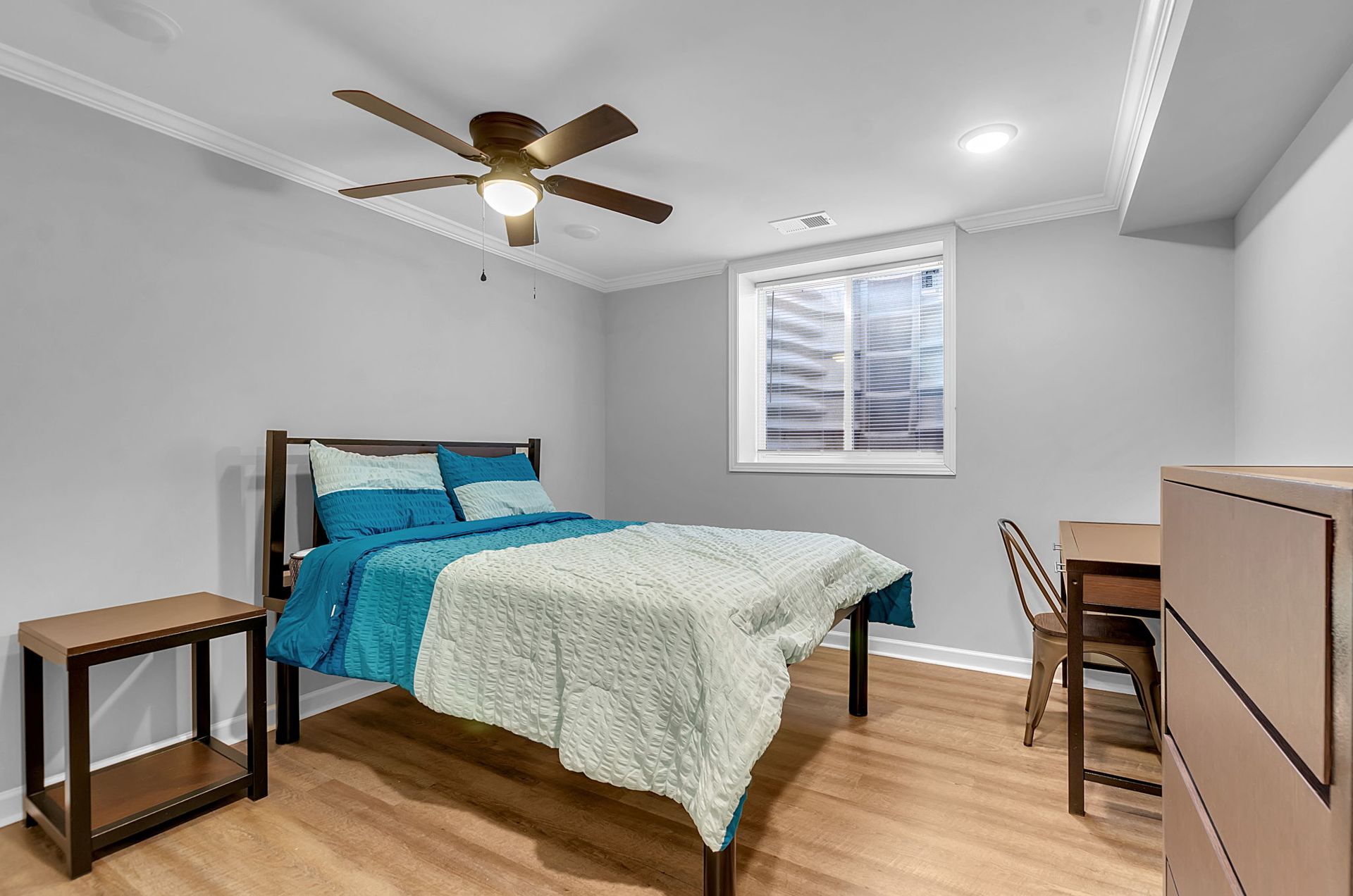 A bedroom with a bed , nightstand , desk and ceiling fan.