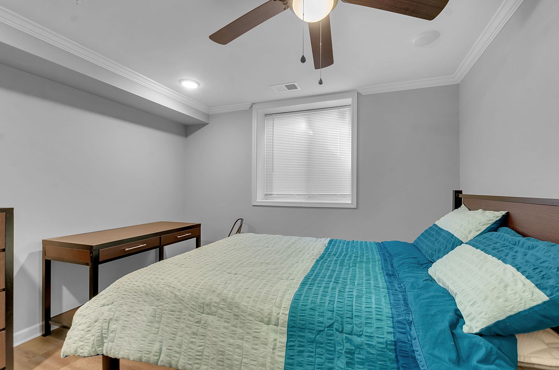 A bedroom with a bed , desk , dresser and ceiling fan.