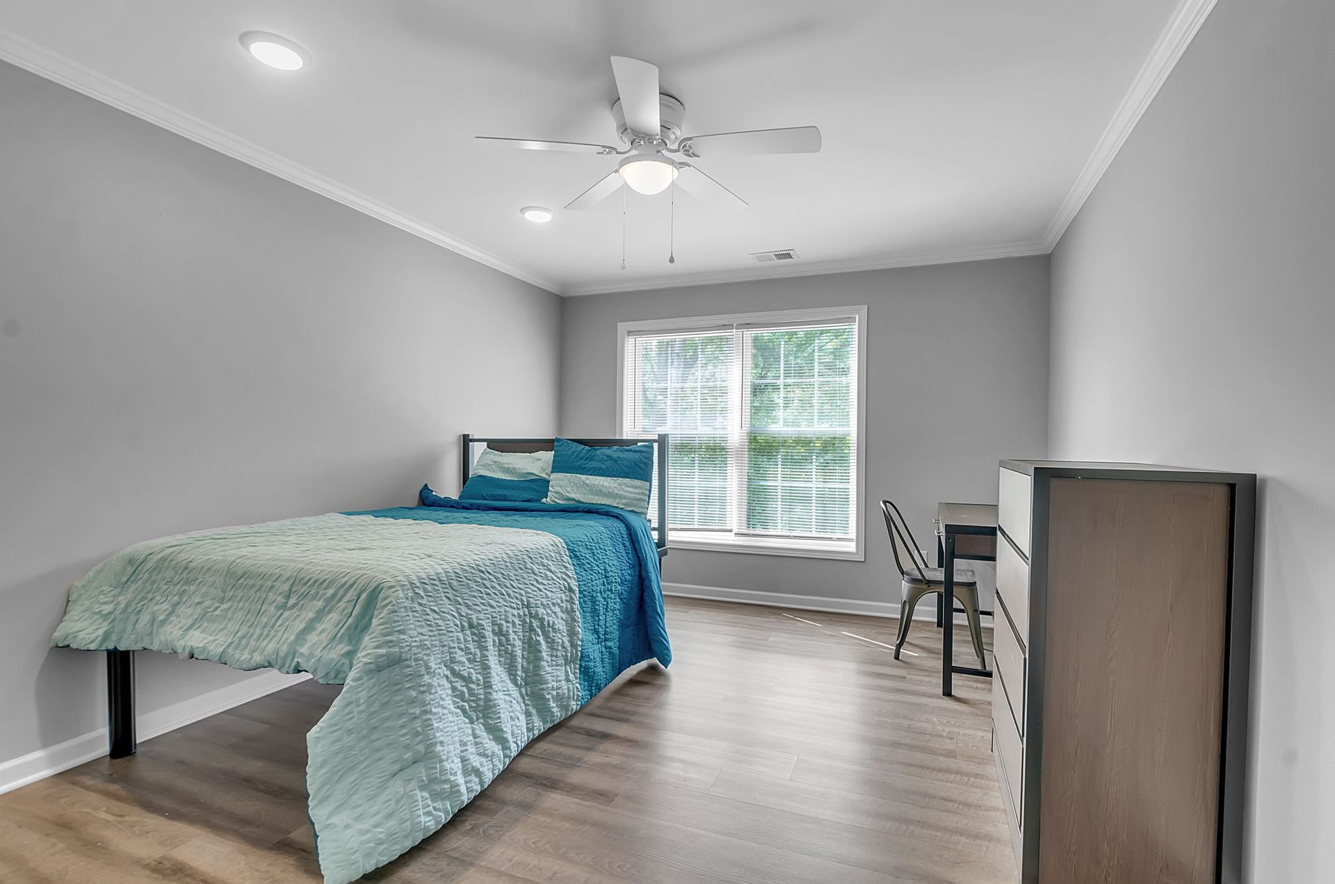 A bedroom with a bed , dresser , desk and ceiling fan.
