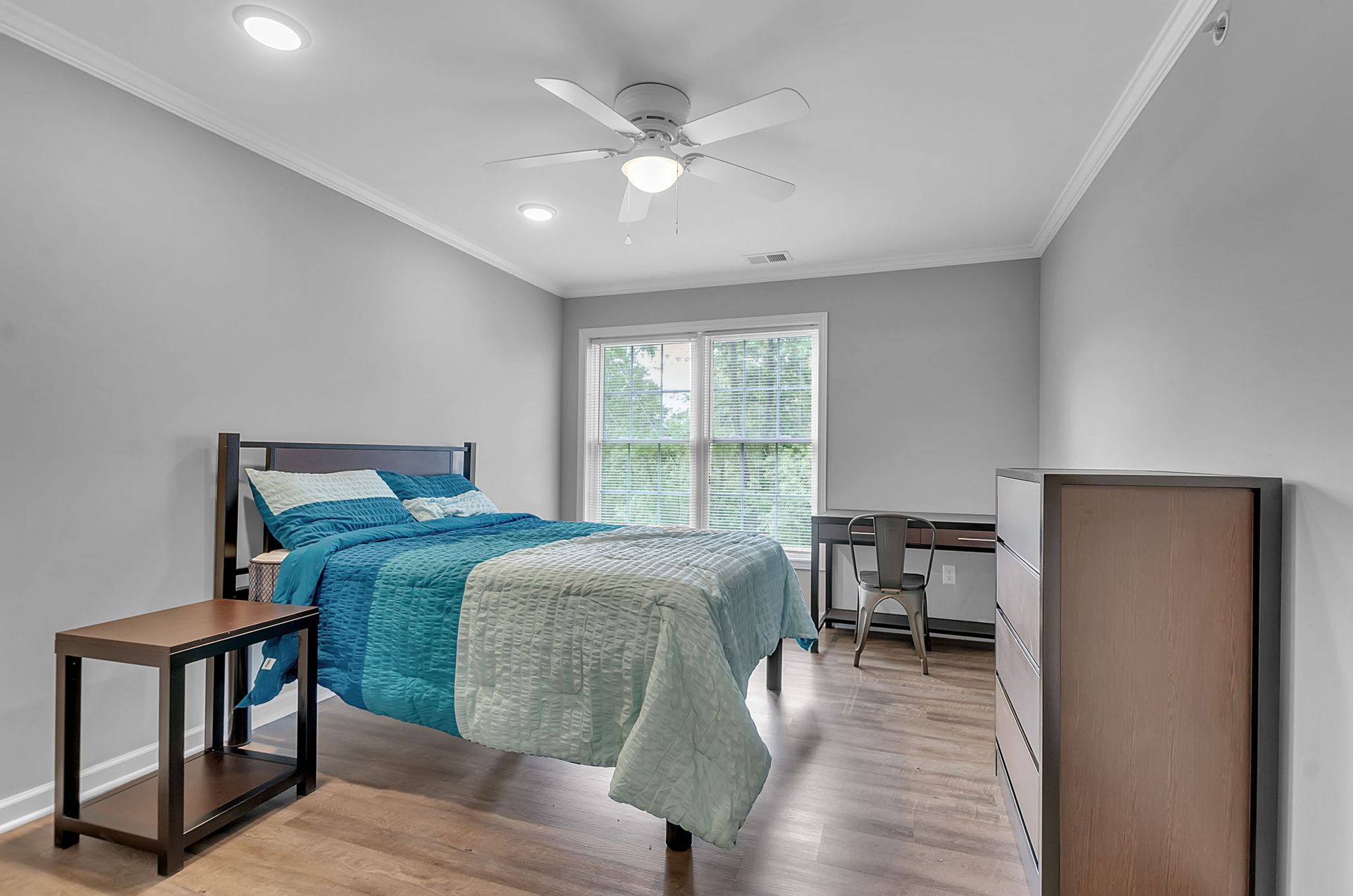 A bedroom with a bed , dresser , desk and ceiling fan.