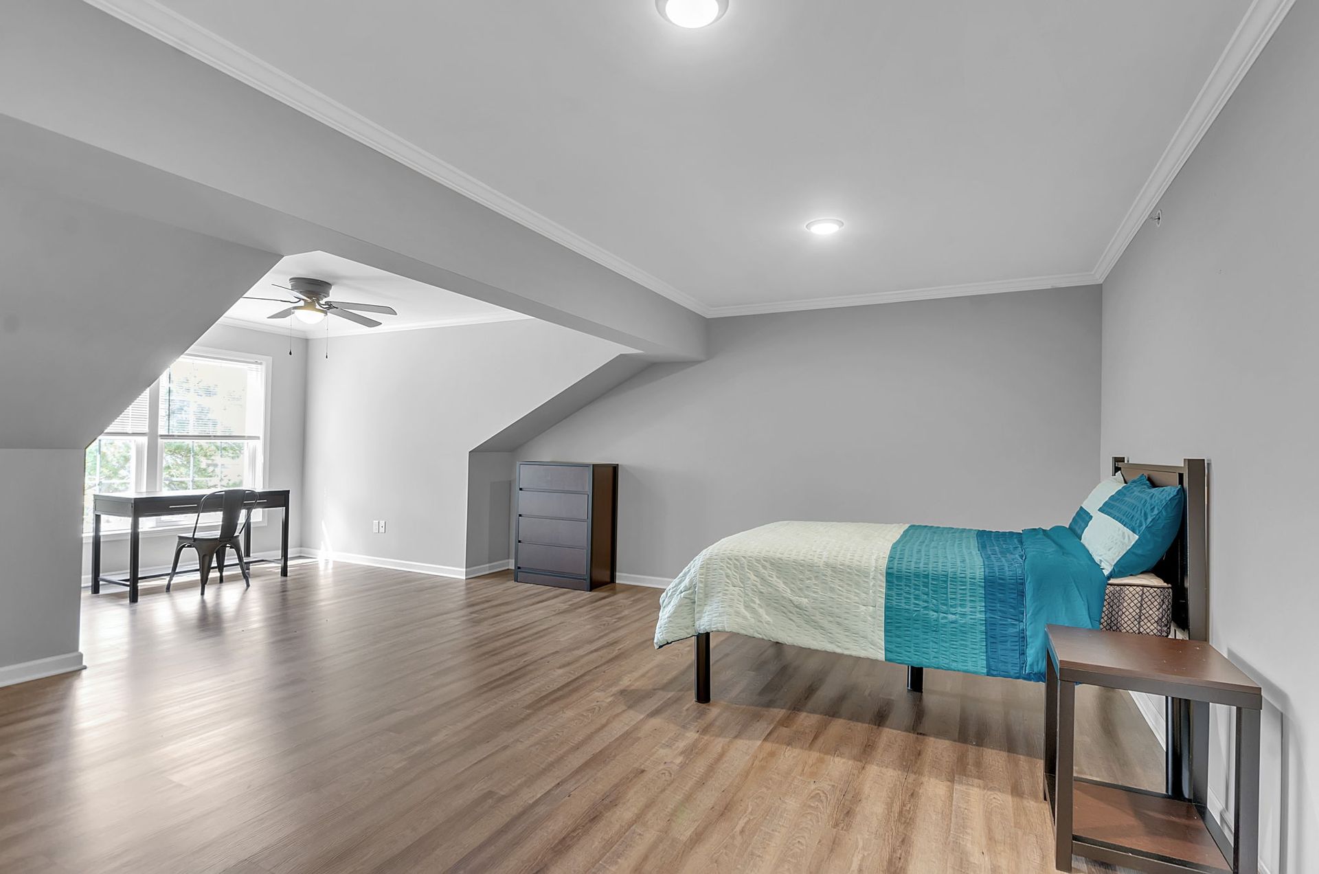 A bedroom with a bed , desk , nightstand and ceiling fan.