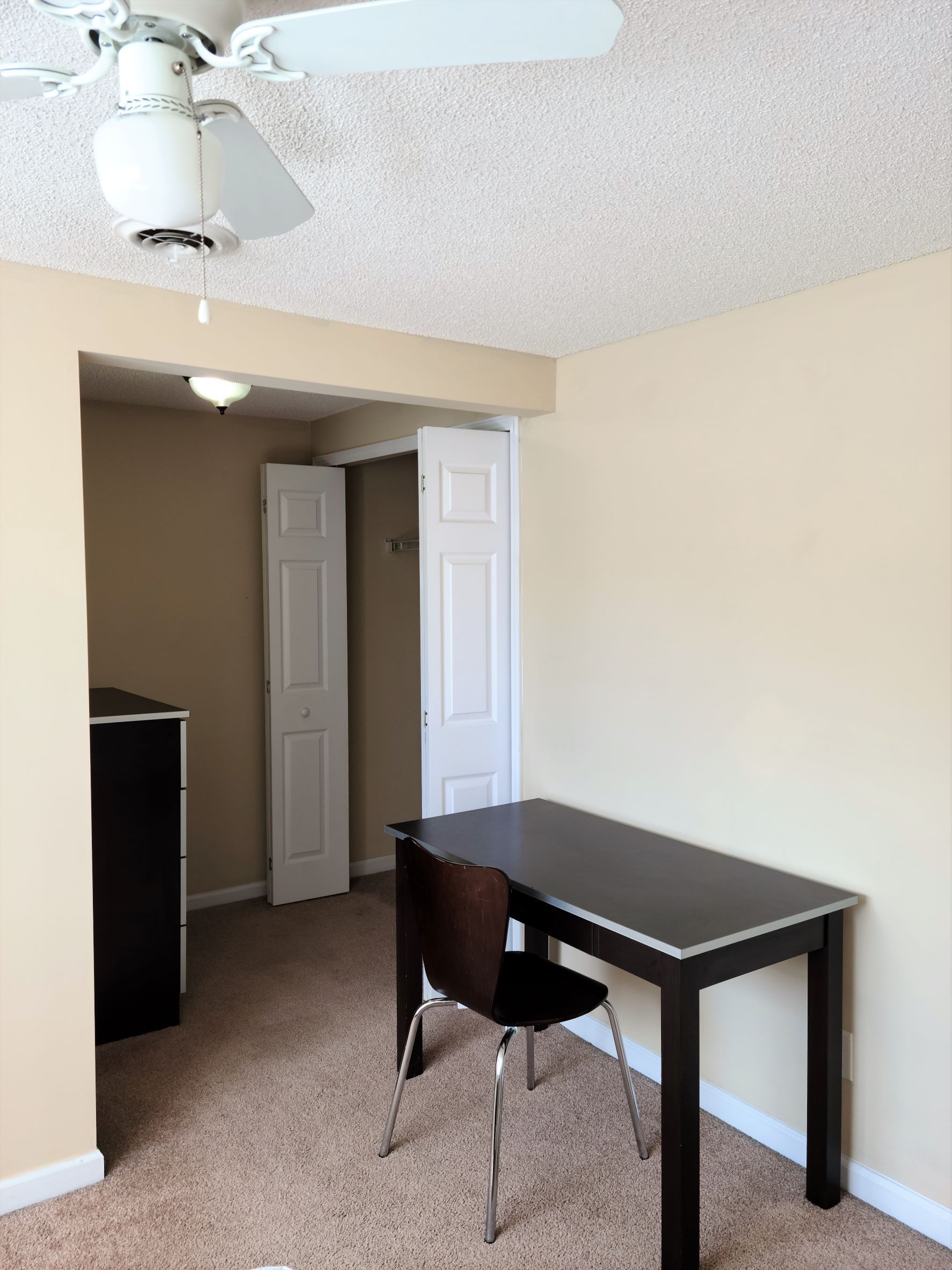 An empty room with a desk and chair under a ceiling fan