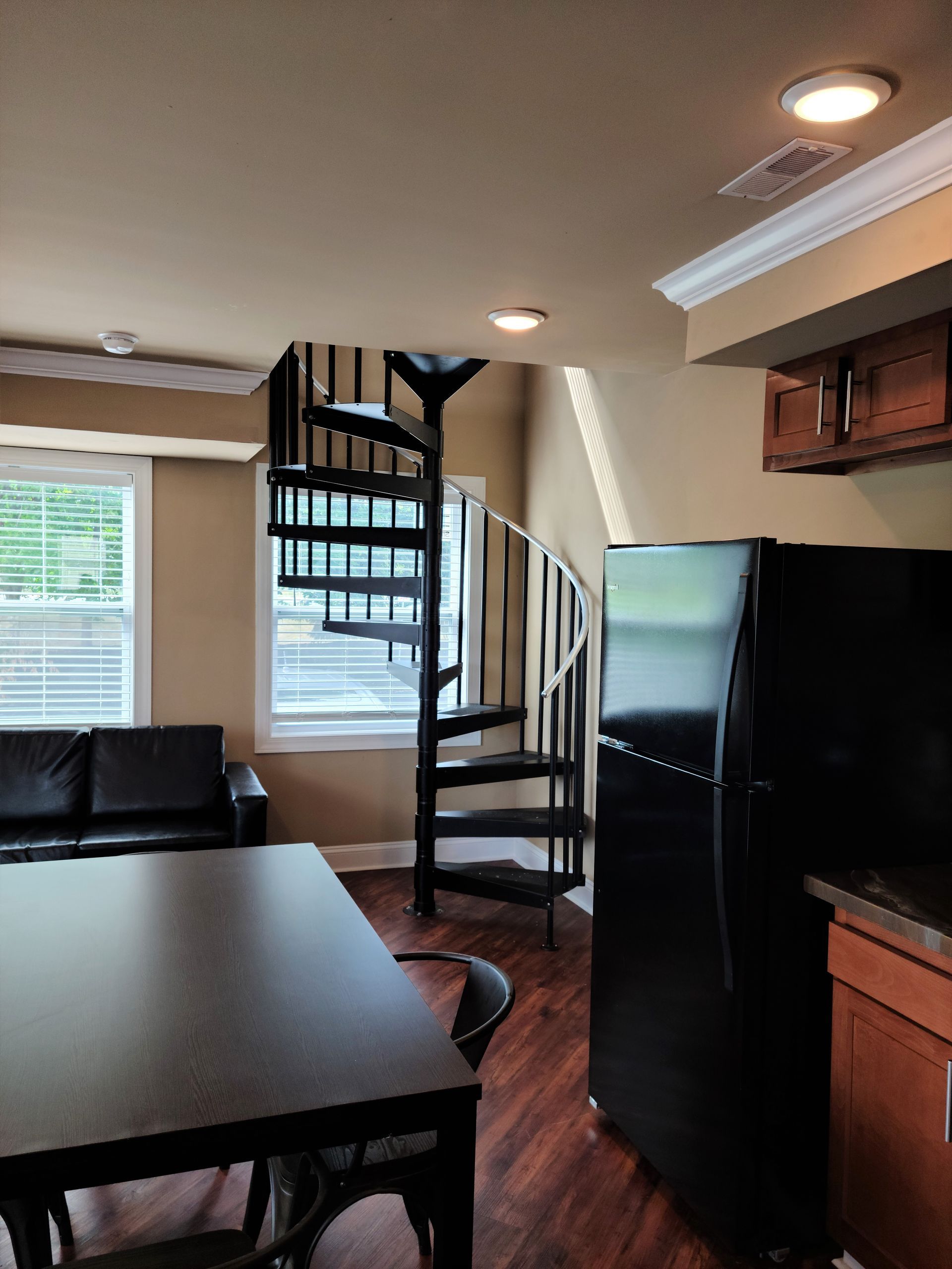 A living room with a spiral staircase and a black refrigerator