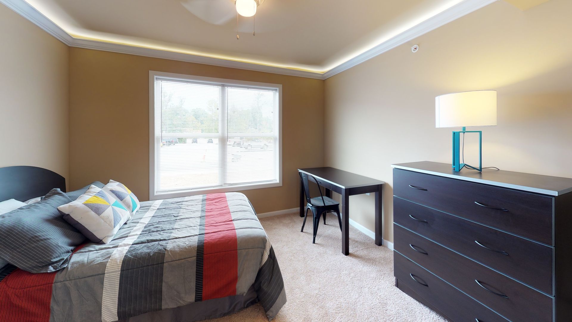 A bedroom with a bed , dresser , desk and window.