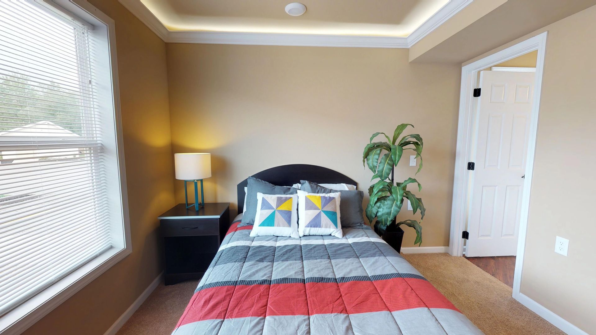 A bedroom with a bed , nightstand , lamp and window.