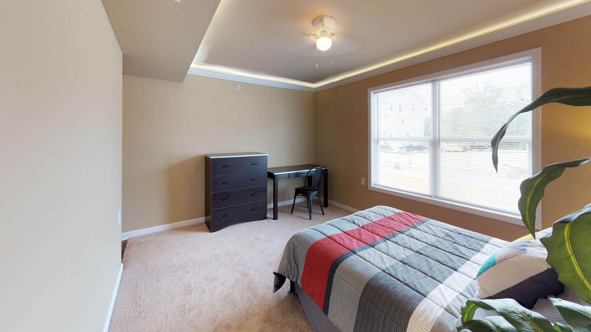 A bedroom with a bed , desk , dresser and two windows.