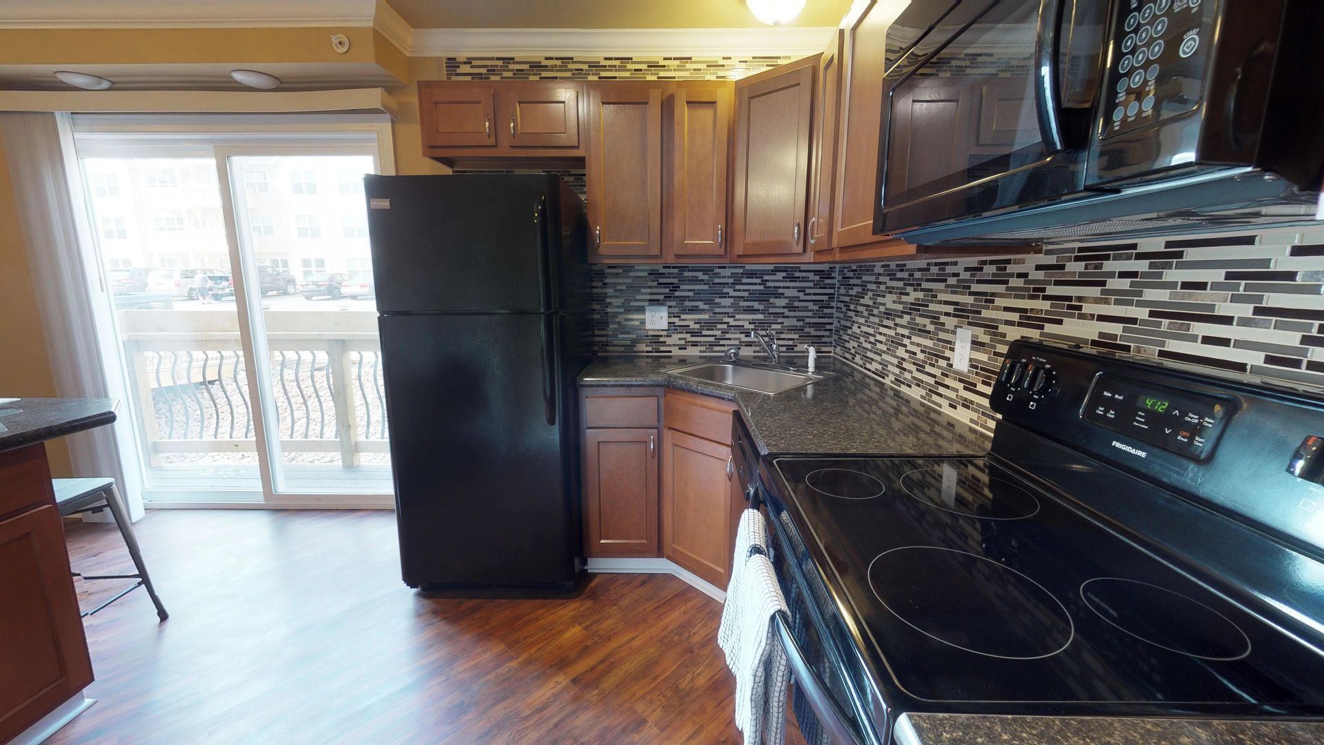 A kitchen with a stove , refrigerator , microwave and sliding glass door.