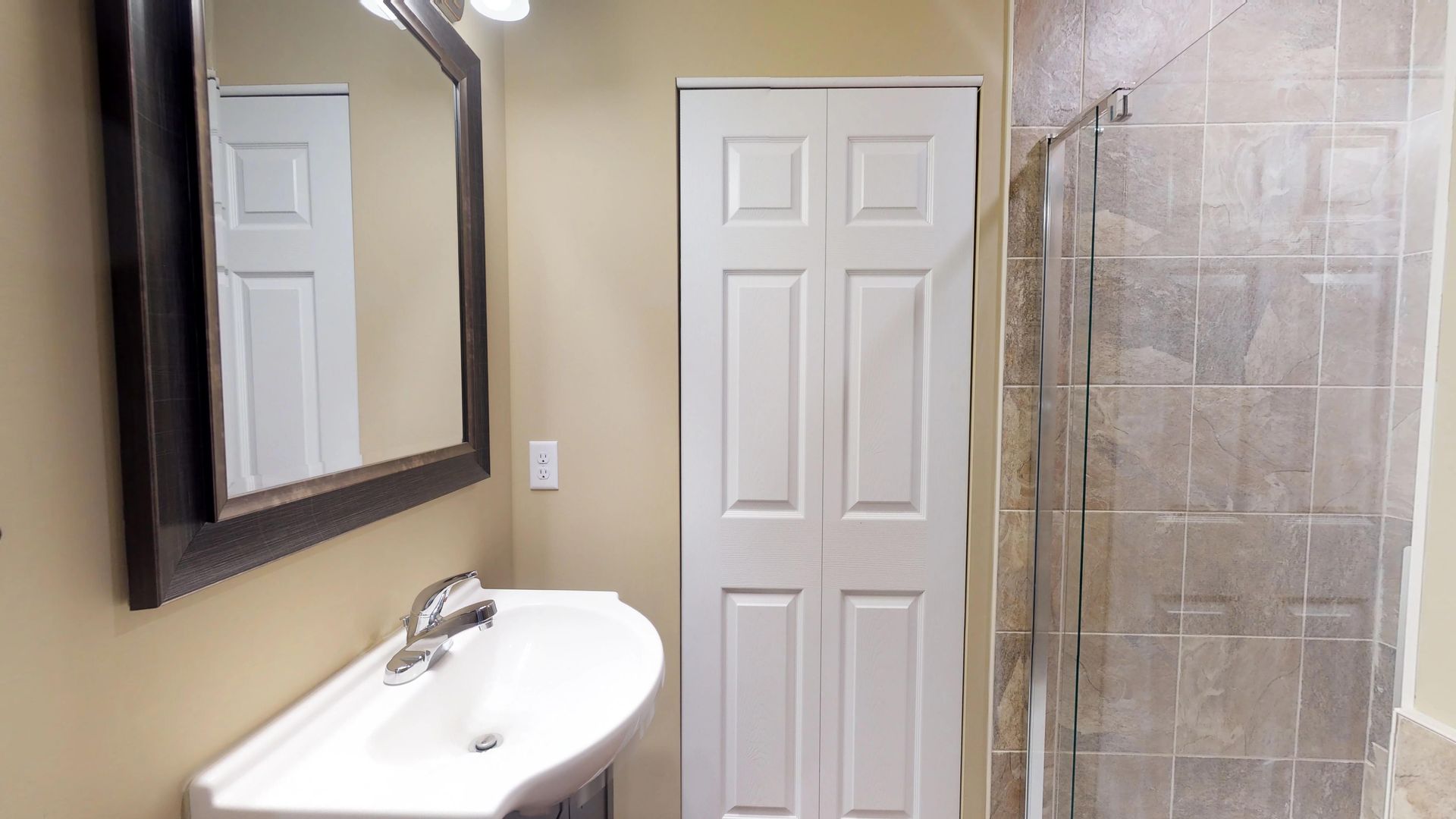 A bathroom with a sink , mirror and walk in shower.