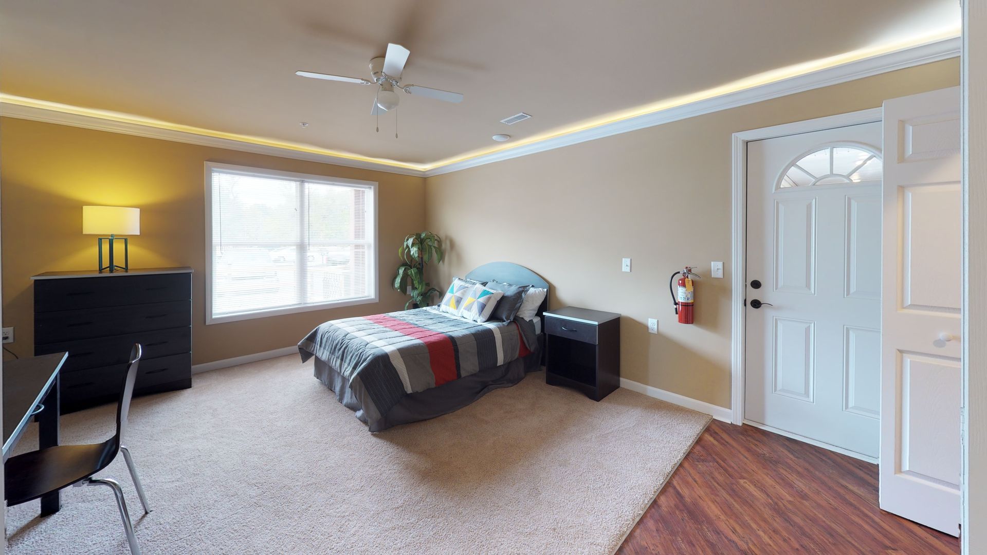 A bedroom with a bed , desk , nightstand , and ceiling fan.