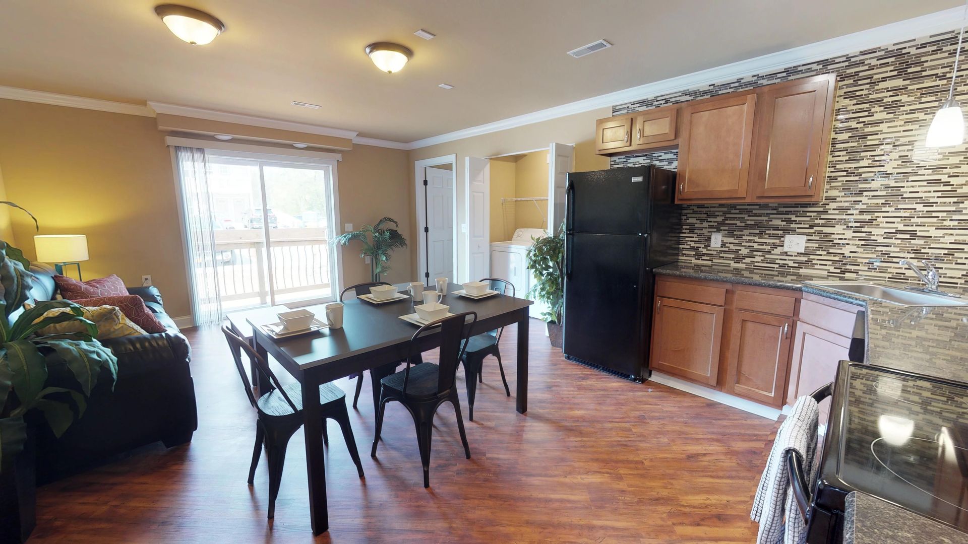A living room with a dining table and chairs and a kitchen with a refrigerator.