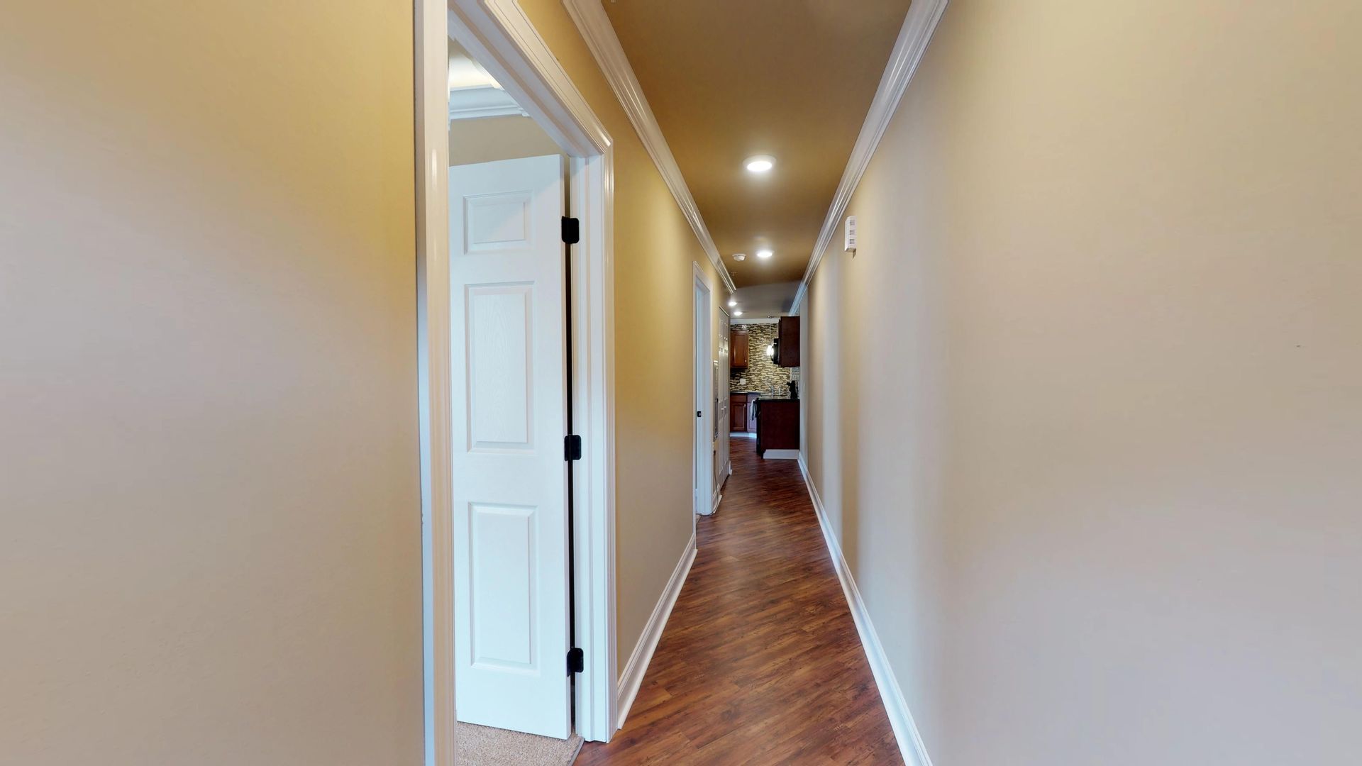 A long hallway with hardwood floors and tan walls in a house.