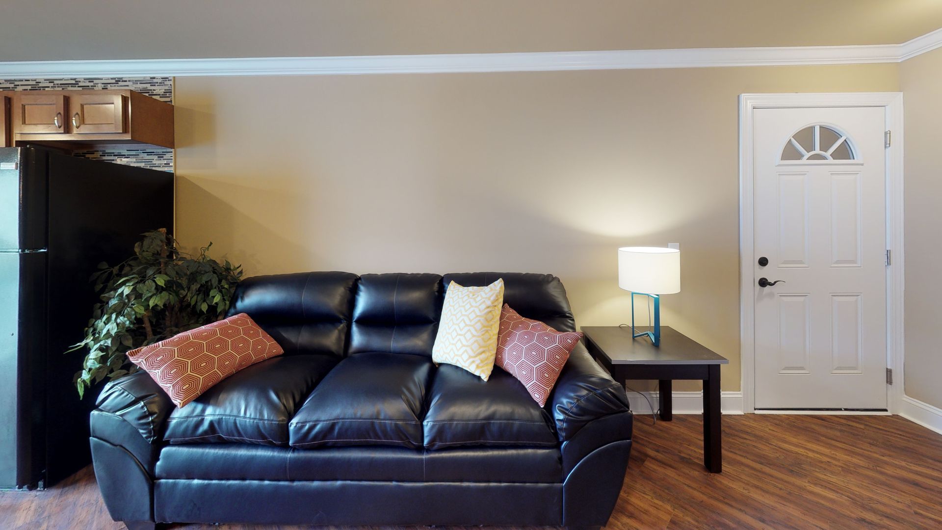 A living room with a black leather couch and a black refrigerator.