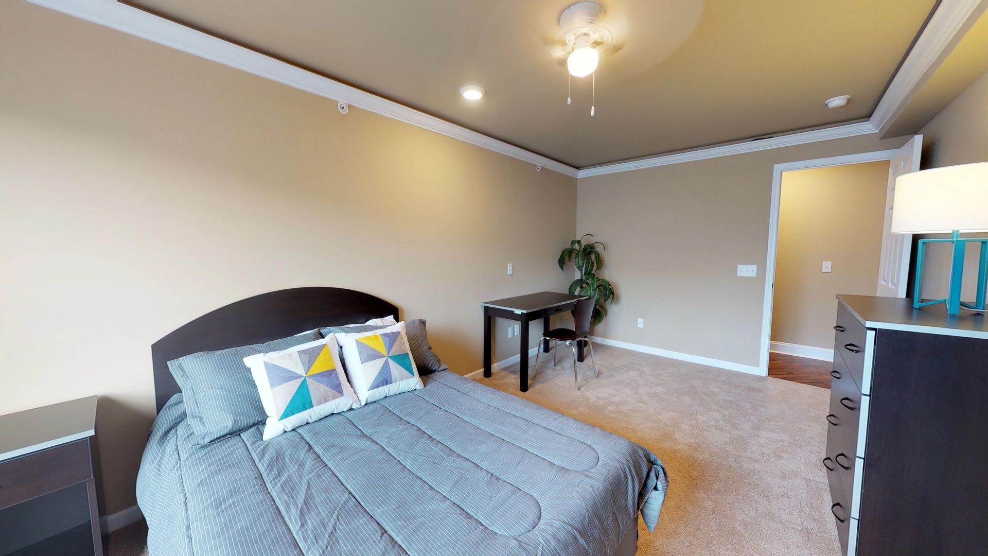 A bedroom with a bed , dresser , desk and lamp.