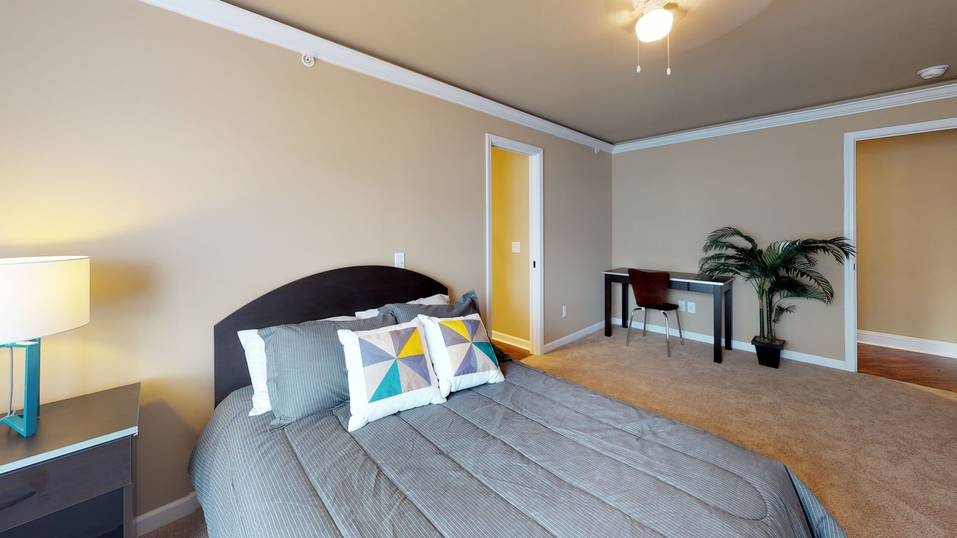 A bedroom with a bed , desk , nightstand and lamp.