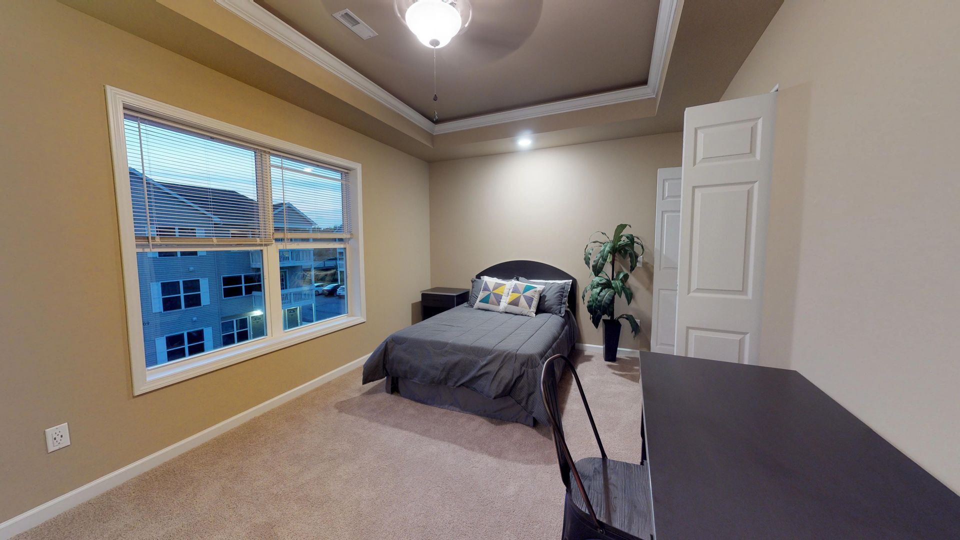 A bedroom with a bed , desk , chair and two windows.