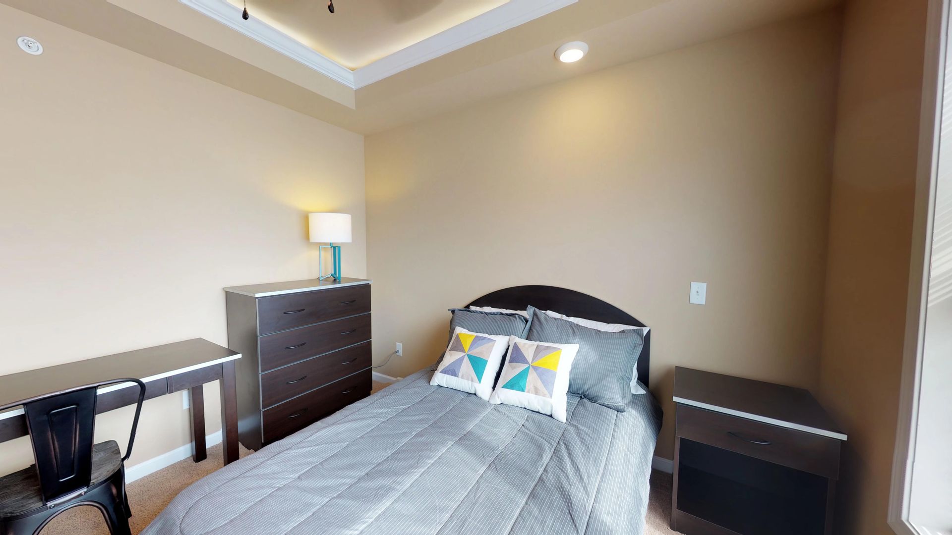 A bedroom with a bed , desk , nightstand and dresser.