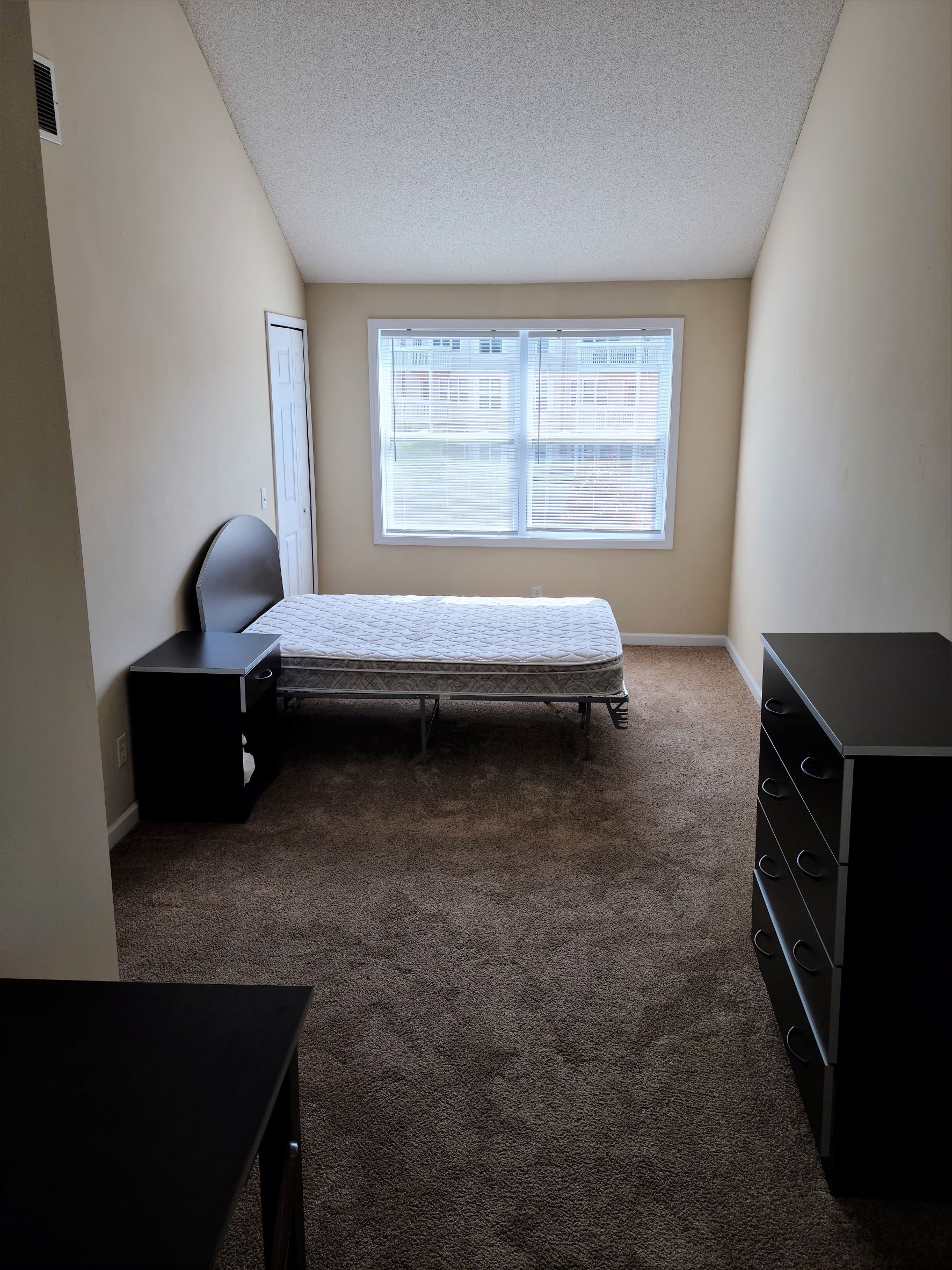 A bedroom with a bed , nightstand , dresser and window.