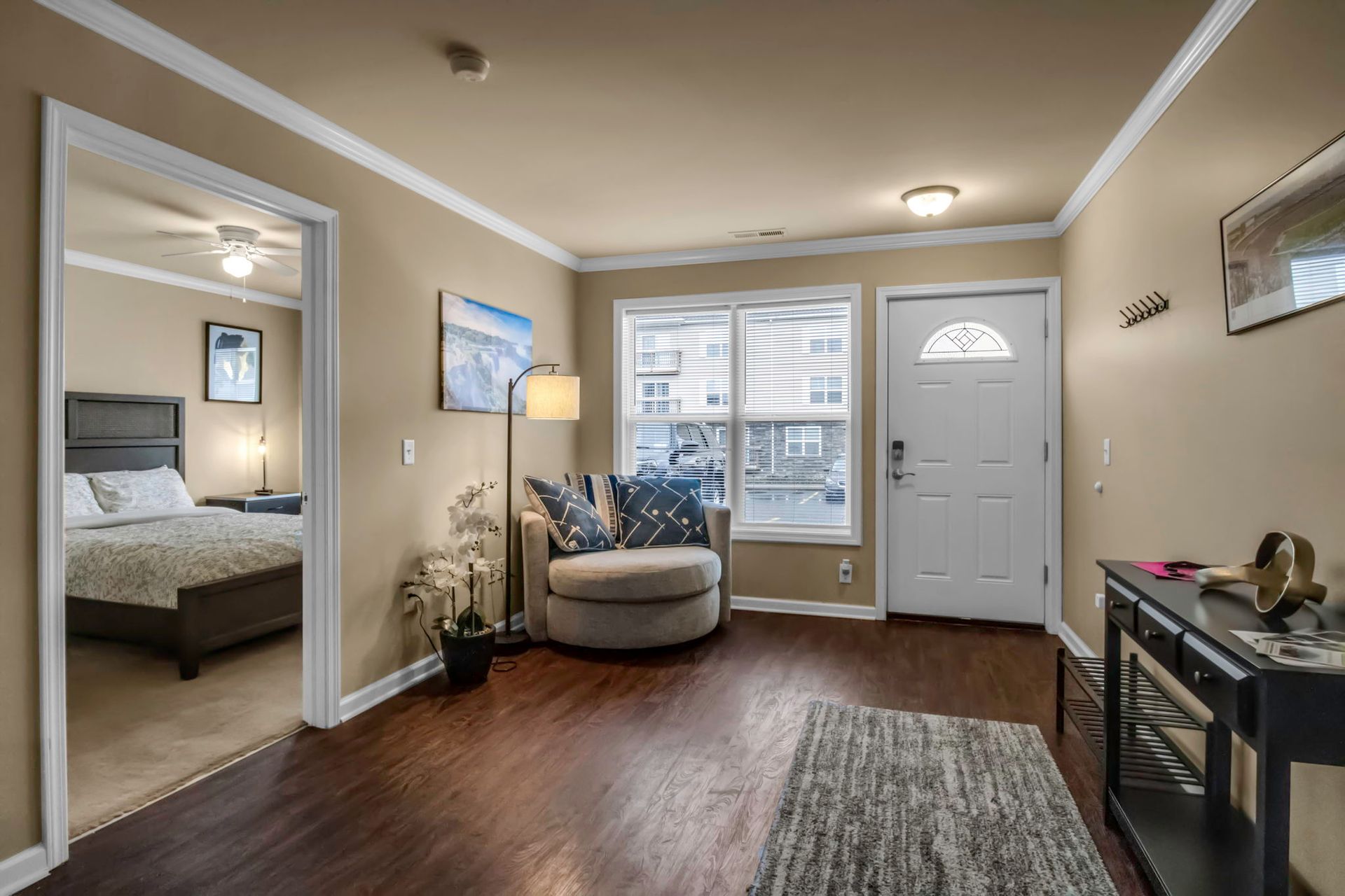 A living room with a chair and a table and a bedroom in the background.