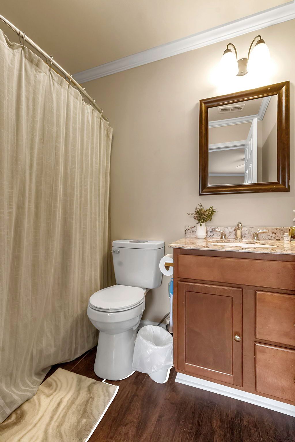A bathroom with a toilet , sink , mirror and shower curtain.
