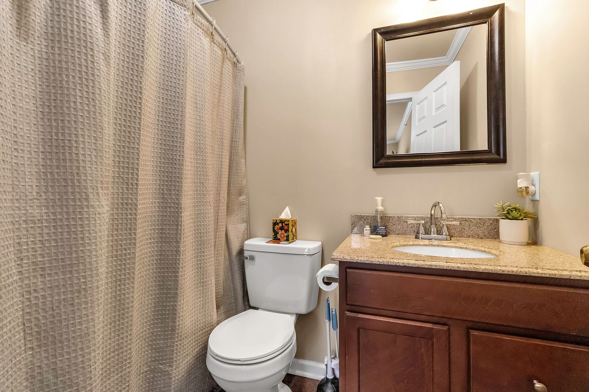 A bathroom with a toilet , sink , mirror and shower curtain.