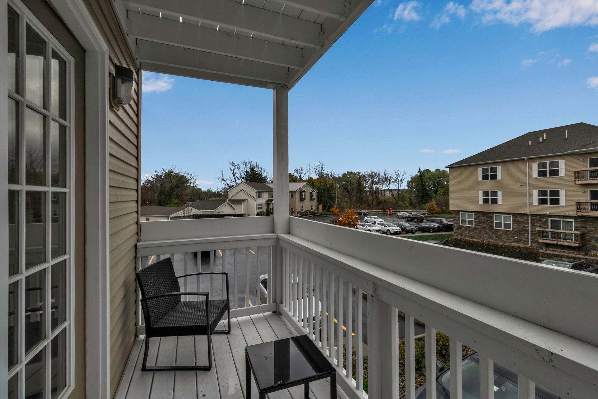 A balcony with a chair and a table overlooking a parking lot