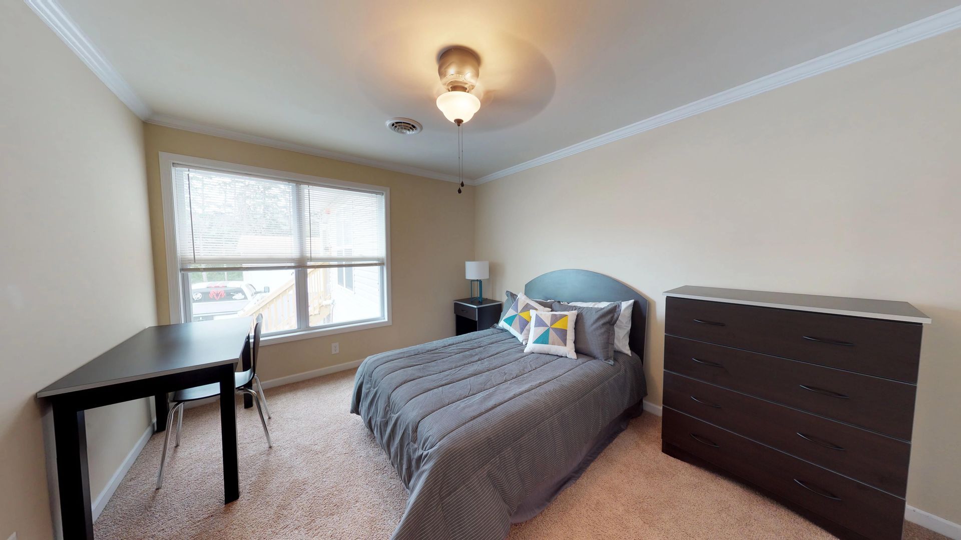 A bedroom with a bed , desk , dresser and window.