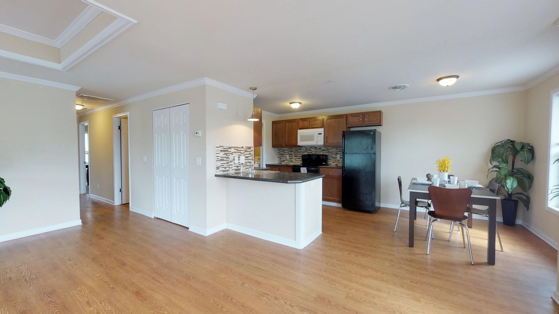 A living room with a table and chairs and a kitchen with a refrigerator.