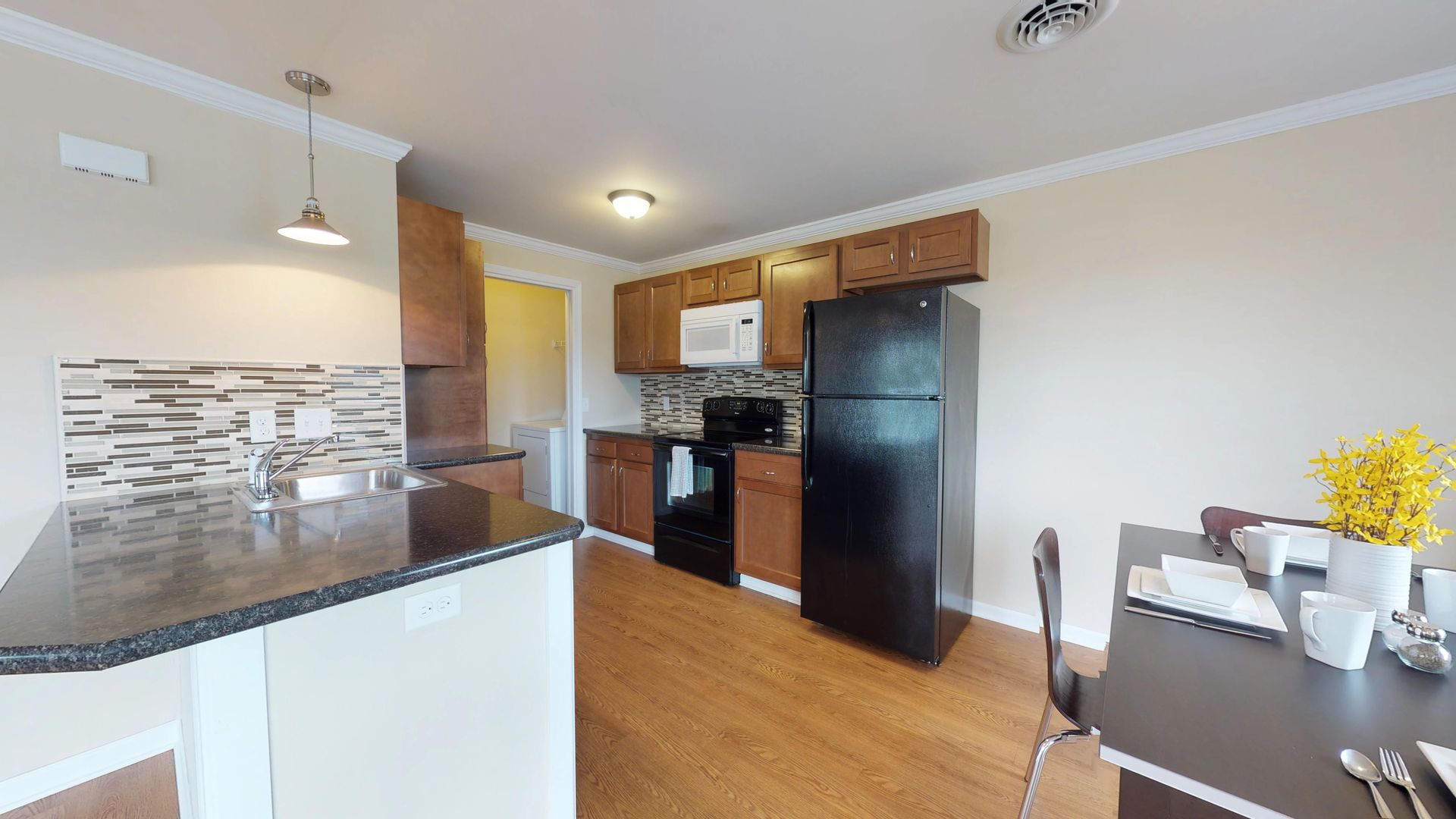 A kitchen with a black refrigerator , stove , sink and table.