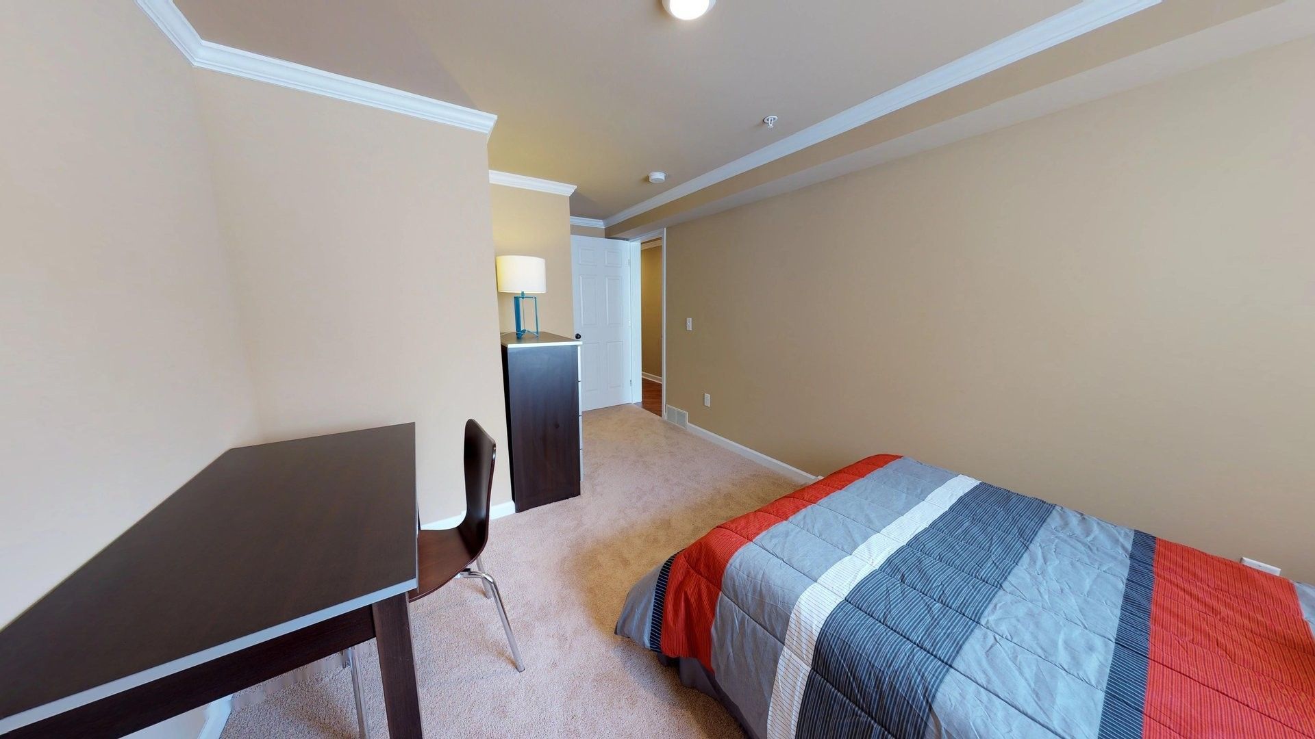A bedroom with a bed , desk , chair and lamp.