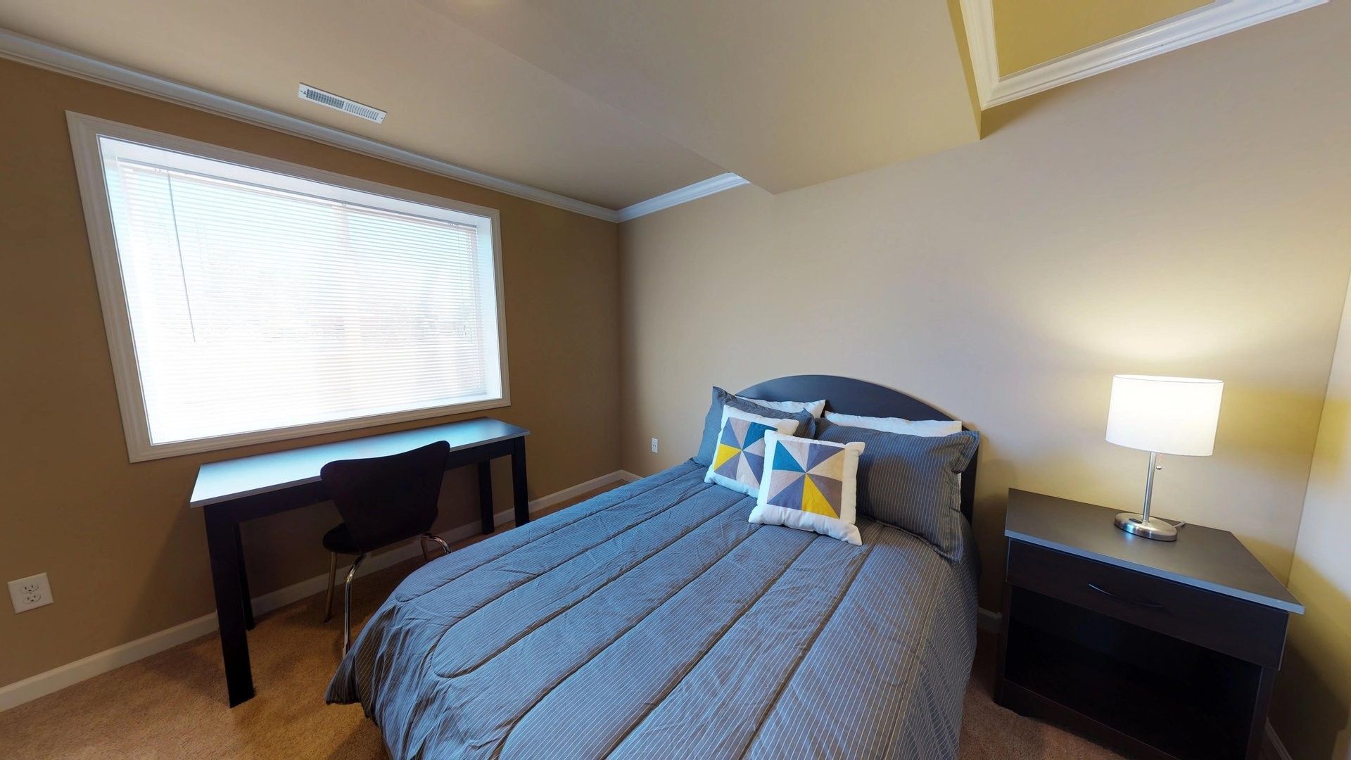 A bedroom with a bed , nightstand , desk and window.